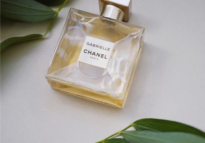 perfume gabrielle chanel, with a essence de perfum with green leafs in the background